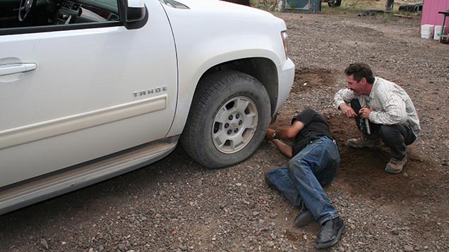 Kevin Schumacher watches as Dust Devil’s Terry Clark labors to fix a flat front tire on the team’s SUV. Kevin Schumacher watches as Dust Devil’s Terry Clark labors to fix a flat front tire on the team’s SUV.