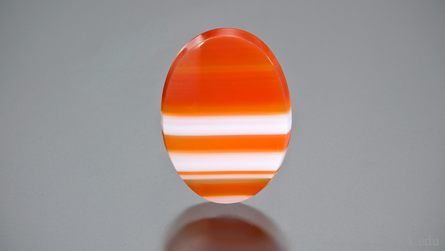 A flat oval polished sardonyx tablet showing the varying orange and white banding of the August birthstone.
