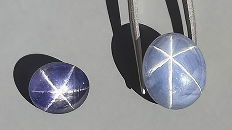 Figure 3. Exceptional star sapphires from Nivithigala, Sri Lanka, viewed in sunlight: a 7.45 ct purple color-change star sapphire (left) and a 19.74 ct light grayish blue star sapphire exhibiting an extraordinarily sharp and distinct star (right). Photo by Jennifer Stone-Sundberg; courtesy of Dudley Blauwet Gems.