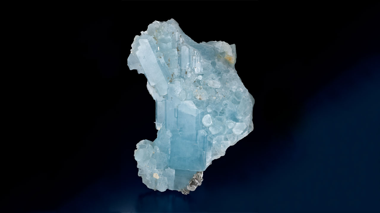 04.Aquamarine_1280x720. An aquamarine crystal group from the Hunza Valley in Pakistan – which weighs more than 2.5 lbs. (1.23 kilograms) – includes some flattened crystals, many that show pyramidal faces, with muscovite. Gift of Roz and Gene Meieran Collection, Phoenix, AZ. Photo by Robert Weldon/GIA