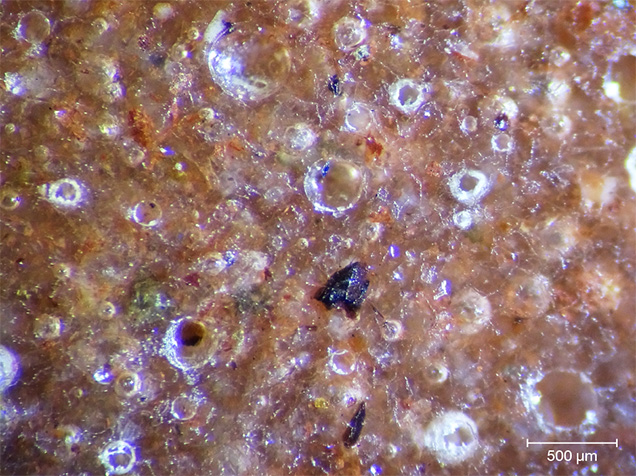 Mineral particles and bubbles in the brown area of the quartz sphere.