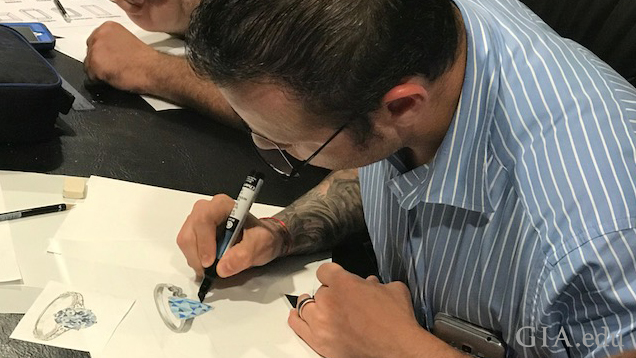 A man works on his drawing of a piece of jewelry.