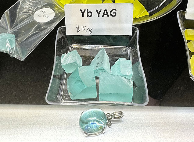 Figure 3. Greenish blue rough and cut ytterbium-doped YAG. The cabochon in front is 14 × 10 mm. Photo by Lisa Kennedy; courtesy of Turtle’s Hoard. Figure 3. Greenish blue rough and cut ytterbium-doped YAG. The cabochon in front is 14 × 10 mm. Photo by Lisa Kennedy; courtesy of Turtle’s Hoard.