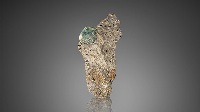 A gem-quality in situ French Bar sill primary sapphire (9 mm long) partially embedded in basaltic trachyandesite rock (sample RK-FBS 001). Photo by Jeff Mason.