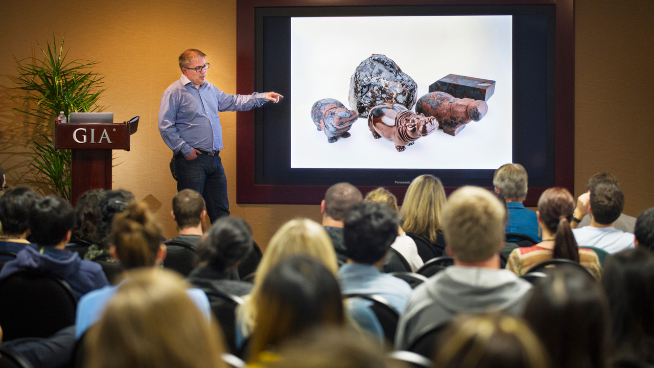 Dreher presented photos of his carvings alongside rough gems to show how he works through each piece to reveal the animal figure. The obsidian hippos pictured on the screen are on display in Carlsbad as part of the “Generations of Mastery” exhibit. Photo by Kevin Schumacher/GIA