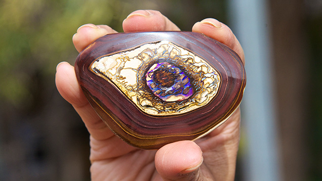 手上拿着砾岩蛋白石. 这块砾岩蛋白石产自大名鼎鼎的矿区 Yowah（犹瓦）小镇。 和黑蛋白石不同，砾岩蛋白石同时含有蛋白石及其母岩。 砾岩蛋白石具有各种各样的形状和图案，这为宝石佩戴者和收藏家带来了更多乐趣，其另一个吸引这些人的特征是含有游彩。 摄影：Andrew Lucas（安德鲁·卢卡斯）/GIA。