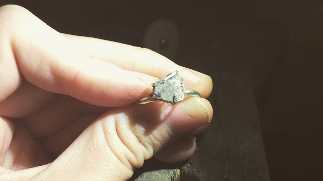 A close up of Grandics’ fingers holding a ring that features a rough diamond.
