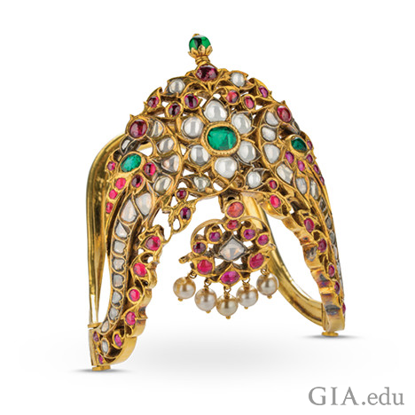 Ornate gold armlet with carvings and featuring diamonds, rubies, emeralds and pearls.
