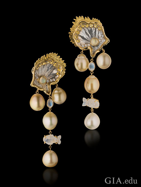 South Sea pearls dangle from clam-shapes made from mother of pearl and accented with white and yellow sapphires and 18K yellow gold. Moonstone accents, including one fish-shaped item, also dangle from the top of the earrings. South Sea pearls dangle from clam-shapes made from mother of pearl and accented with white and yellow sapphires and 18K yellow gold. Moonstone accents, including one fish-shaped item, also dangle from the top of the earrings.