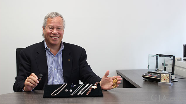 Man sits at his desk with a display stand of multiple pieces of jewelry in front of him. Man sits at his desk with a display stand of multiple pieces of jewelry in front of him.