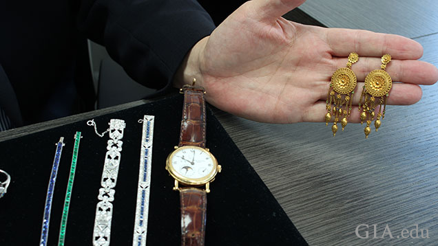 A tray of jewelry pieces sits on the desk and a hand holds a pair of Castellani earrings. A tray of jewelry pieces sits on the desk and a hand holds a pair of Castellani earrings.