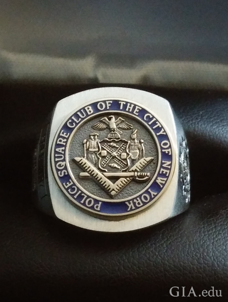 A square shaped ring with a circular center with raised symbols. It is engraved with “Police Square Club of the City of New York.” A square shaped ring with a circular center with raised symbols. It is engraved with “Police Square Club of the City of New York.”