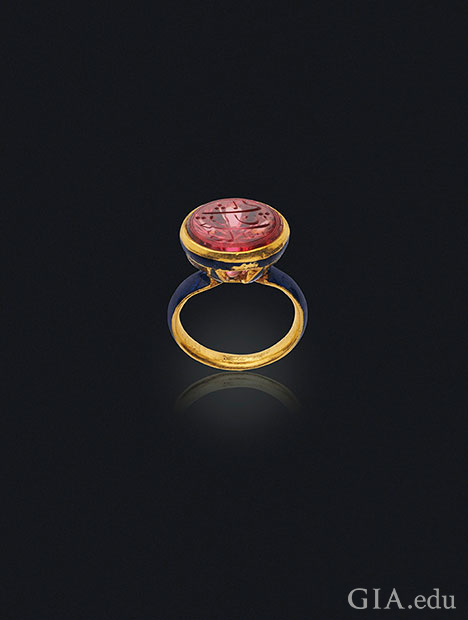 A carved spinel sits on the top of an enamel seal ring.