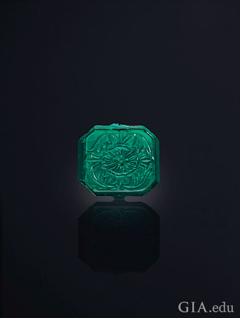 A square shaped emerald with carving on top.