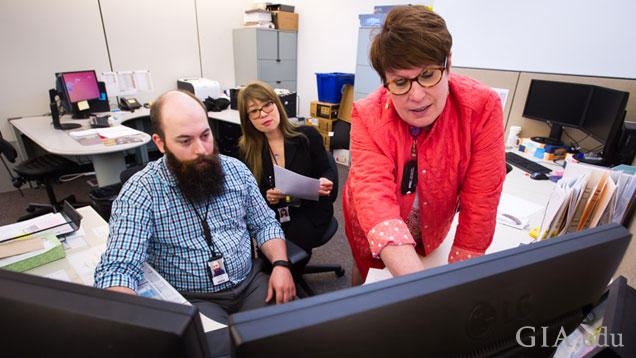 Three jewelry manufacturing arts team members (2 seated, one standing) in front of two large computer monitors. Three jewelry manufacturing arts team members (2 seated, one standing) in front of two large computer monitors.