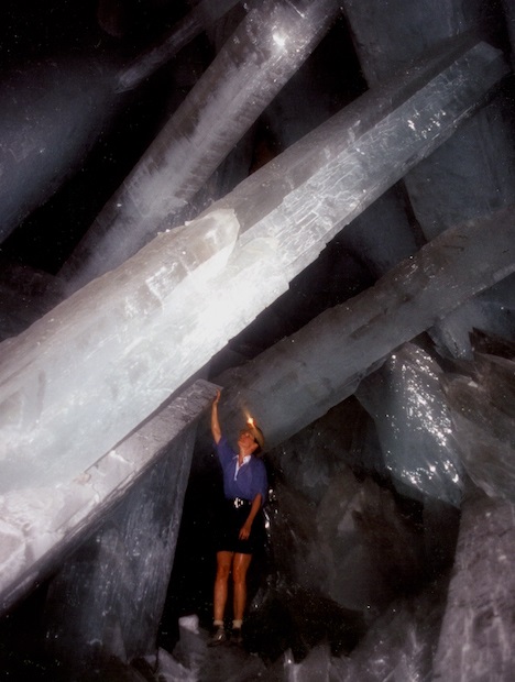 Huge crystals tower above and around woman in a dark cave. Huge crystals tower above and around woman in a dark cave.