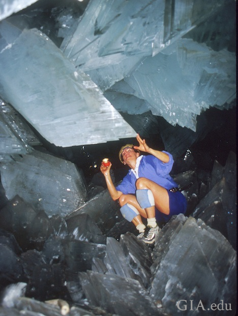 Woman sits amidst sharp, huge crystals in a cave. Woman sits amidst sharp, huge crystals in a cave.