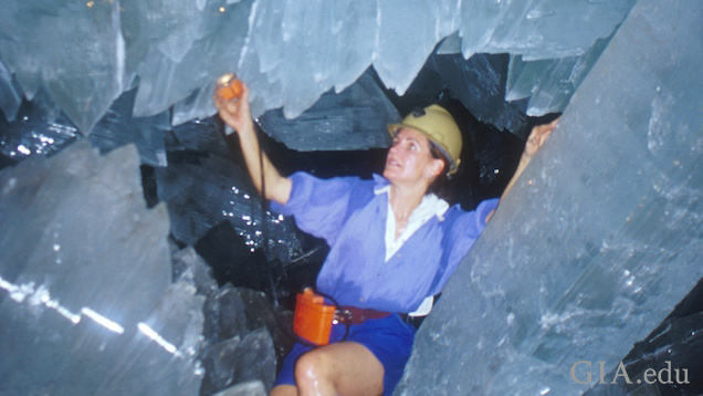 Woman shines a light on huge crystals as she crawls among them. Woman shines a light on huge crystals as she crawls among them.
