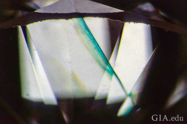 This cleavage crack shows a bright green “flash effect” when observed subparallel to the plane of the break against a bright background. This is diagnostic of clarity enhancement in diamonds. Field of view 3.20 mm. This cleavage crack shows a bright green “flash effect” when observed subparallel to the plane of the break against a bright background. This is diagnostic of clarity enhancement in diamonds. Field of view 3.20 mm.