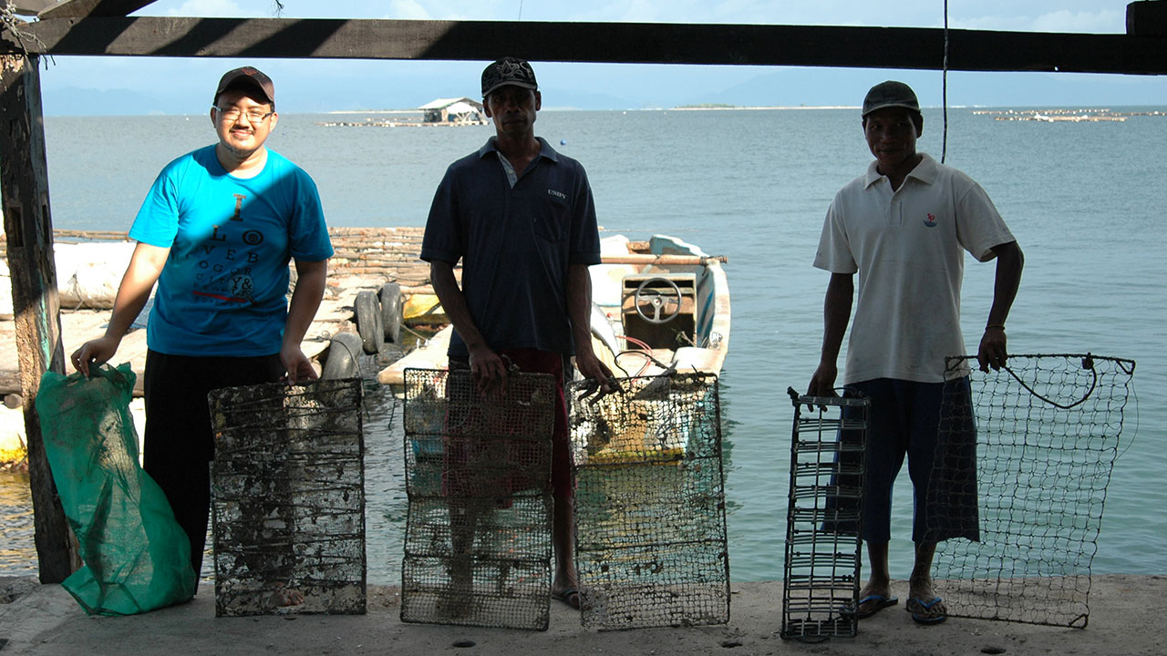 FA16-Sturman-Gallery-8_208489-1280x720.jpg. Mohamad Irfan Bin Ansori (left) with two of the Lombok farm hands showing the different sizes of mollusk holders used. The green holder Mohamad holds is for spat, while the one on the far right is for adults. Photo by Nicholas Sturman.