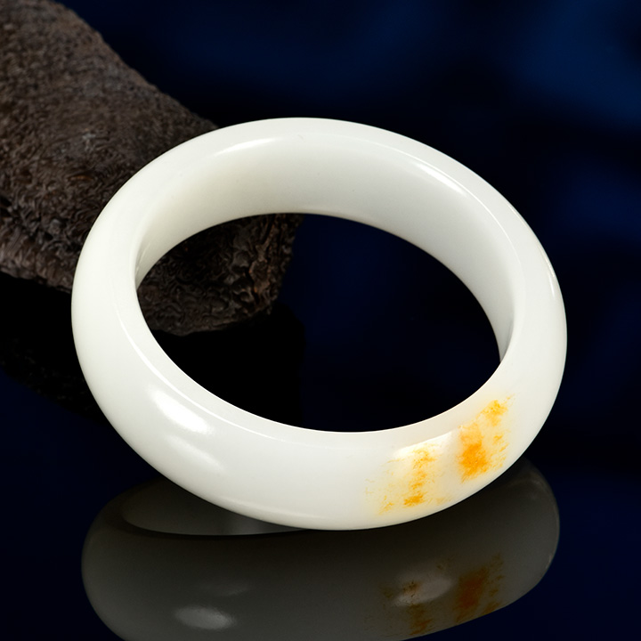 Figure 1. A high-quality Russian white nephrite bracelet, measuring approximately 58 × 13 × 7 mm, with the orange peel effect observable in its reflective areas. Photo by Zuojiang Chen. Figure 1. A high-quality Russian white nephrite bracelet, measuring approximately 58 × 13 × 7 mm, with the orange peel effect observable in its reflective areas. Photo by Zuojiang Chen.