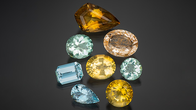 Figure 1. Some of Virtu Gem’s larger gemstones from Kenya, Malawi, and Zambia at the Ethical Gem Fair. Clockwise from top: 45.00 ct citrine, 32.33 ct rutilated quartz, 9.80 ct aquamarine, 21.65 ct citrine, 9.99 ct aquamarine, 12.32 ct aquamarine, 17.20 ct aquamarine, and 20.15 ct citrine (center). Photo by Robert Weldon; courtesy of Virtu Gem.