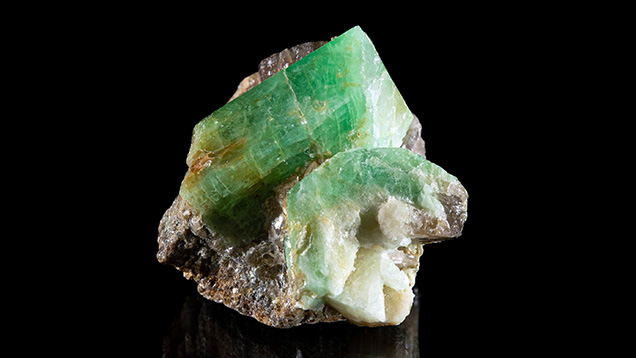 Figure 2. In situ emerald and beryl from Newfoundland. The primary crystal shows a lively green hue. The crystal on the lower right shows strong concentric zonation with a green rim and a white core. Photo by Emma Hutchinson Photography; courtesy of Art Gardner. Figure 2. In situ emerald and beryl from Newfoundland. The primary crystal shows a lively green hue. The crystal on the lower right shows strong concentric zonation with a green rim and a white core. Photo by Emma Hutchinson Photography; courtesy of Art Gardner.