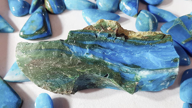 Figure 2. Rough sample of Chilean blue opal, about 18 cm wide, displaying a dull conchoidal fracture, alternating green and blue bands, some white lenses (milky quartz), and a light brown matrix. Photo by Cristiano Brigida; courtesy of Chilean Rocks and Minerals. Figure 2. Rough sample of Chilean blue opal, about 18 cm wide, displaying a dull conchoidal fracture, alternating green and blue bands, some white lenses (milky quartz), and a light brown matrix. Photo by Cristiano Brigida; courtesy of Chilean Rocks and Minerals.