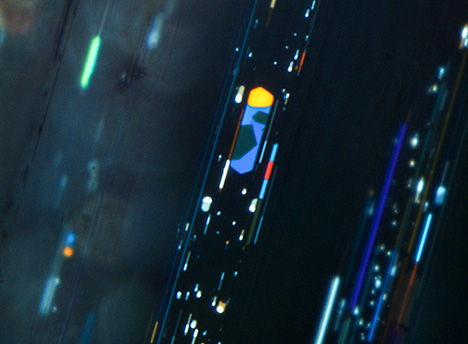 Iridescent platy voids in phenakite under oblique fiber-optic illumination. Iridescent platy voids in phenakite under oblique fiber-optic illumination.