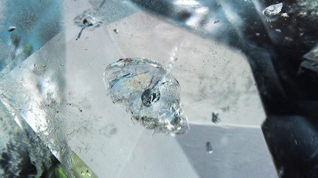 Figure 3. Disk-shaped fissures in the aquamarine were caused by solid inclusions in the middle with tubular fissures extending inward. Photomicrograph by Yubing Chen; field of view 1.50 mm. Figure 3. Disk-shaped fissures in the aquamarine were caused by solid inclusions in the middle with tubular fissures extending inward. Photomicrograph by Yubing Chen; field of view 1.50 mm.