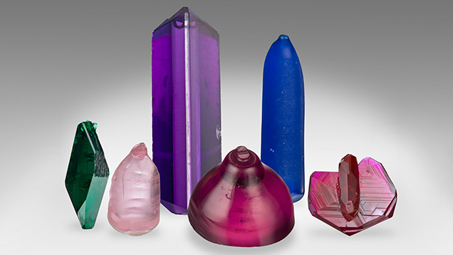 Figure 16. Synthetic crystals from the GIA Museum collection. Left to right: Russian hydrothermal synthetic emerald, flame-fusion pink synthetic spinel, hydrothermal synthetic amethyst with a colorless seed plate, titanium-doped Czochralski-grown purplish pink synthetic sapphire boule, flame-fusion blue synthetic spinel boule, and flux-grown Ramaura synthetic ruby. Photos by Robert Weldon.