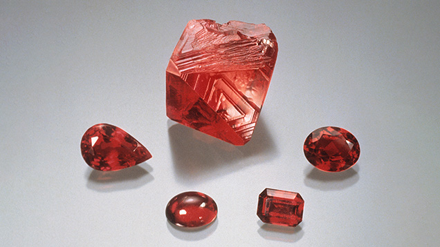 Figure 6. Flux-grown synthetic ruby produced by the Douros method. The rough rhombohedral crystal weighs 44.74 ct, and the cut stones range from 2.14 to 4.93 ct. Photo by Robert Weldon; courtesy of John Douros.