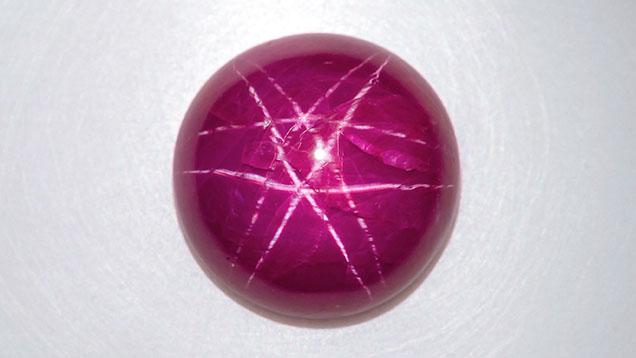 Figure 1. This unheated 11.43 ct purplish red round ruby cabochon displayed a white double-star phenomenon. Photo by Nuttapol Kitdee.