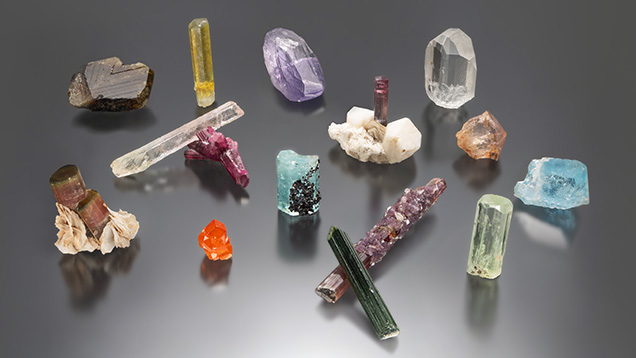 Figure 1. A selection of pegmatite gem crystals, including beryl, chrysoberyl, garnet, spodumene, topaz, and tourmaline. Photo by Mimi Travis; courtesy of the GIA Museum collection.