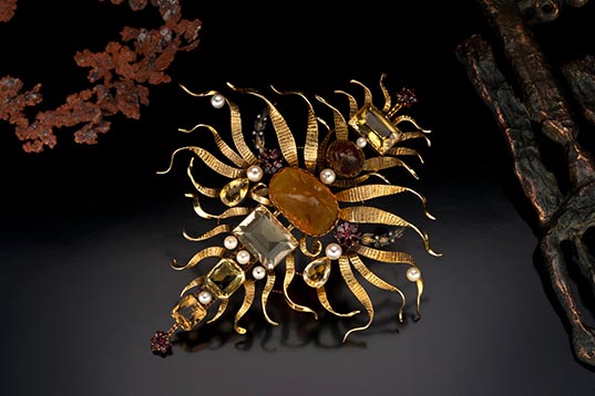 Solar-Motive-brooch-636x358.jpg. This brooch is made of Baltic amber, citrine, garnet, cultured pearl, seed pearl, 18K gold. Courtesy of The Anthony and Elizabeth Duquette Foundation for the Living Arts.