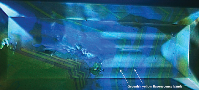 Figure 2. Alternating blue and greenish yellow fluorescence zones were observed with deep-UV excitation. This fluorescence pattern is typical for diamonds colored by the 480 nm visible absorption band. Image by Stephanie Shaw. Figure 2. Alternating blue and greenish yellow fluorescence zones were observed with deep-UV excitation. This fluorescence pattern is typical for diamonds colored by the 480 nm visible absorption band. Image by Stephanie Shaw.