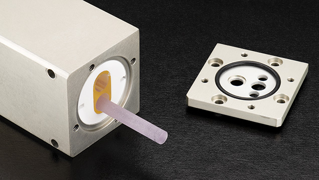 Figure 3. The laser head of one of the 213 nm laser ablation systems used at GIA. In this system, a Nd:YAG rod is housed in a chamber along with a xenon flash lamp that stimulates the production of 1064 nm fluorescence from the Nd:YAG. This fluorescence is frequency-quintupled to 213 nm light and focused into a laser. Photo by Emily Lane. Figure 3. The laser head of one of the 213 nm laser ablation systems used at GIA. In this system, a Nd:YAG rod is housed in a chamber along with a xenon flash lamp that stimulates the production of 1064 nm fluorescence from the Nd:YAG. This fluorescence is frequency-quintupled to 213 nm light and focused into a laser. Photo by Emily Lane.