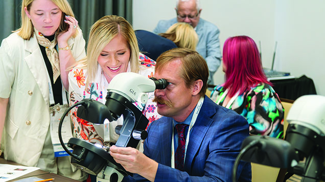 Figure 3. Aaron Palke helps orient a treated gemstone under the microscope for seminar attendees to view its diagnostic inclusions. Photo by Emily Lane. Figure 3. Aaron Palke helps orient a treated gemstone under the microscope for seminar attendees to view its diagnostic inclusions. Photo by Emily Lane.