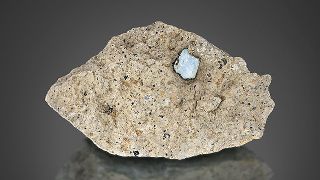 Figure 11. A sapphire (8 mm in length) in French Bar sill matrix rock showing a thin biotite (phlogopite) coating (RK-FBS 003). To be preserved as an attractive mineral specimen, enough matrix surrounding the sapphire is removed. Photo by Jeff Mason. Figure 11. A sapphire (8 mm in length) in French Bar sill matrix rock showing a thin biotite (phlogopite) coating (RK-FBS 003). To be preserved as an attractive mineral specimen, enough matrix surrounding the sapphire is removed. Photo by Jeff Mason.