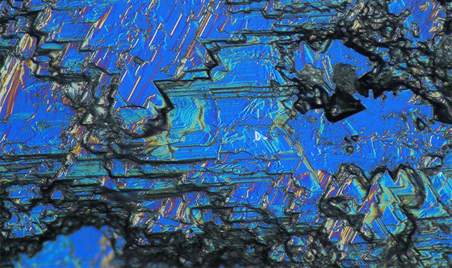 Figure 18. French Bar sill sapphires show a variety of different resorption features, also called etching or dissolution. In this sapphire (RK-FBS 041), differential interference contrast (DIC) photomicrography shows angular geometric patterns reflecting disequilibrium with the carrier magma during its volcanic transport to the surface. Photomicrograph by Aaron Palke; field of view 0.52 mm. Figure 18. French Bar sill sapphires show a variety of different resorption features, also called etching or dissolution. In this sapphire (RK-FBS 041), differential interference contrast (DIC) photomicrography shows angular geometric patterns reflecting disequilibrium with the carrier magma during its volcanic transport to the surface. Photomicrograph by Aaron Palke; field of view 0.52 mm.
