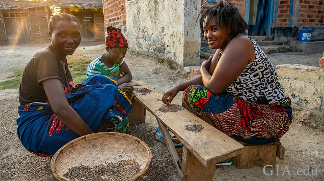 Three woman sit on the ground around a low bench/table to sort through gravel for gems. Three woman sit on the ground around a low bench/table to sort through gravel for gems.