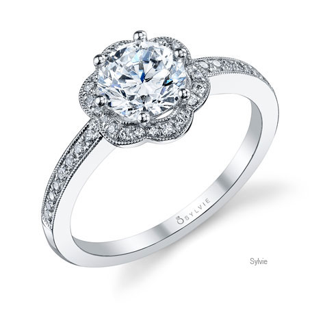 Perspective view of platinum ring designed by Sylvie, featuring a flower-shaped diamond halo surrounding a large center diamond, and diamonds set halfway down the shank. Perspective view of platinum ring designed by Sylvie, featuring a flower-shaped diamond halo surrounding a large center diamond, and diamonds set halfway down the shank.