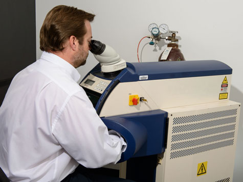 Practitioner seated at the laser welder, welding a platinum ring