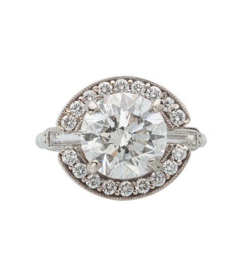 Top view of a platinum solitaire ring containing a round brilliant center diamond and baguette side diamonds. A white gold halo set with small round Top view of a platinum solitaire ring containing a round brilliant center diamond and baguette side diamonds. A white gold halo set with small round