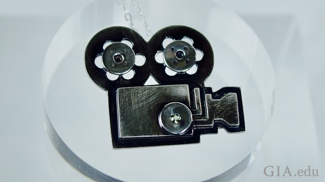 A black sterling silver pendant of a movie camera and film reels. A black sterling silver pendant of a movie camera and film reels.