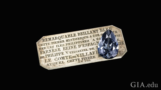 A large pear shaped diamond sits on a silver plaque with French words. A large pear shaped diamond sits on a silver plaque with French words.
