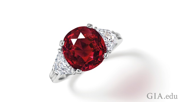 A round ruby is flanked by diamonds in a ring.