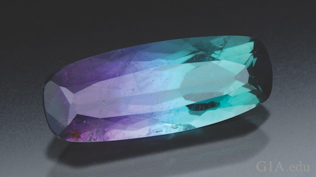 An elongated rectangular cut tourmaline displays shades of purple and tourquoise.